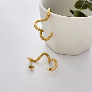 Close-up of golden irregular wavy hoop earrings with smooth fluid texture on a white cup
