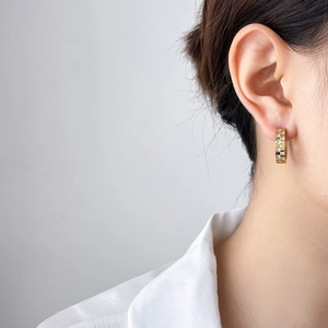 Detail of gold huggie earrings featuring checkerboard zircon inlays on model