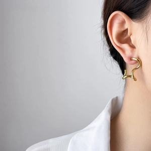 Close-up of wavy gold-toned geometric earrings with high-polish finish on a model