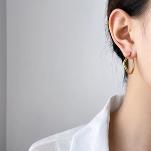 Close-up of a model wearing minimalist irregular golden wave hoop earrings in titanium steel