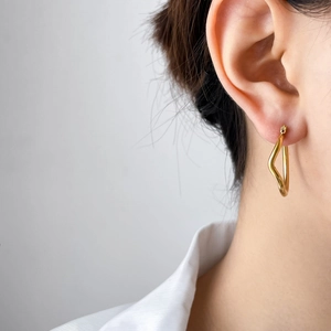 Close-up of golden irregular geometric twist earrings on model showing minimalist style