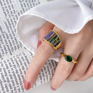 Goldene Ringe mit grünen Zirkonia und Muscheleinlage auf einem Buch präsentiert