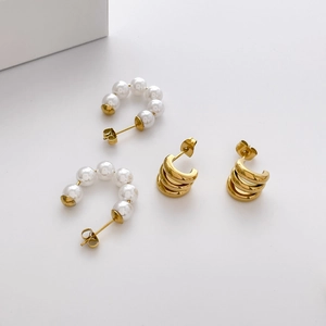 Detail of C-shaped pearl studs and triple-layered gold hoop earrings on white surface
