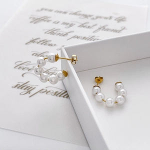 Detailed close-up of C-shaped pearl drop earrings featuring multiple white pearls on gold posts