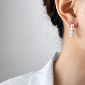 Detail of five white pearls arranged in a curve on a gold stud earring worn by a model
