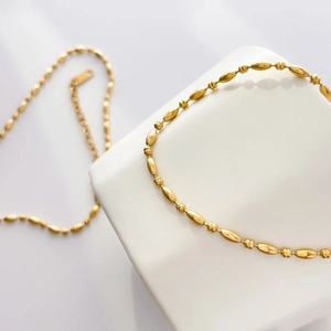 Detail of 18k gold plated titanium steel chain with oval and round beads on white decor