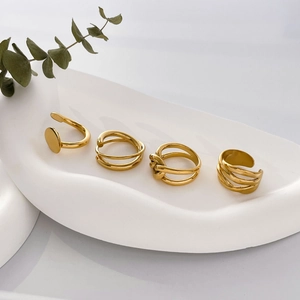 Set of four minimalist gold plated geometric rings with twist and wave patterns on ceramic tray