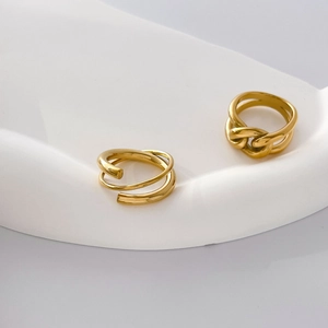 Close-up of gold-plated chunky chain and spiral rings on a white minimalist pedestal