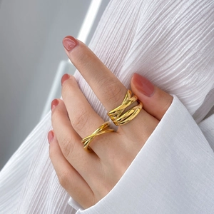 Detail of layered gold-plated chunky ring and minimalist thin cross line band on hand