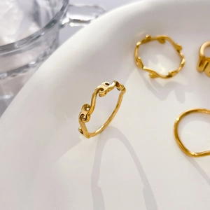 Close-up of minimalist wave gold rings with organic lines on white ceramic tray