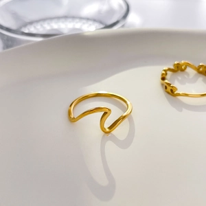 Detail of gold-plated rings with wave and hollow chain designs on white ceramic