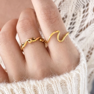 Macro shot of two polished golden wave rings styled with a cream knit sweater