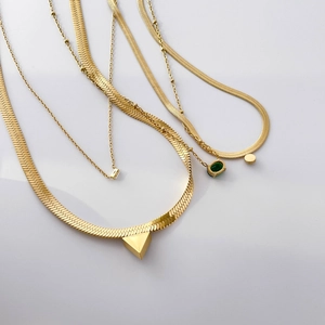 Detail of layered gold herringbone chain with green emerald oval and triangle pendants