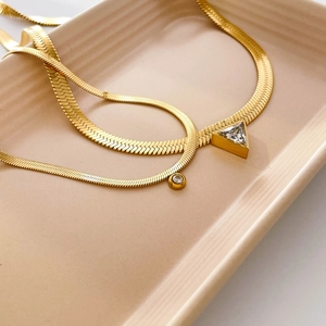 Gold snake chain necklace with triangular zircon and round crystal pendants on a tray