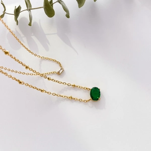 Detailed close-up of gold beaded chain necklace with emerald green oval and square gemstones