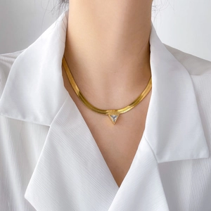 Detail of a gold snake chain necklace with a triangular zircon pendant on a model