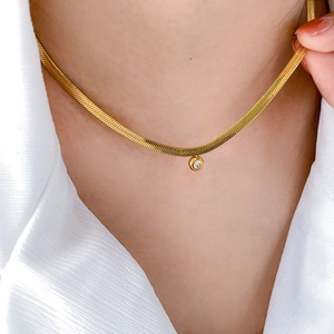 Close-up of golden flat snake chain necklace with a round sparkling zircon pendant