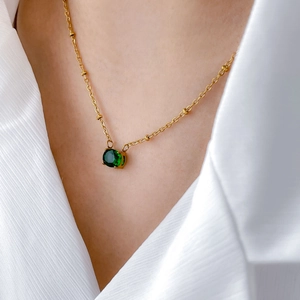Close-up of gold chain necklace with green zircon pendant on a white shirt