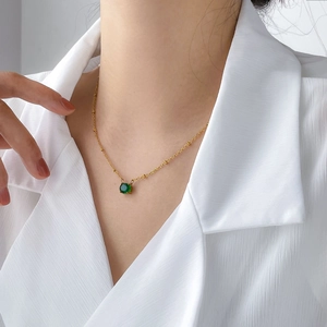 Detail shot of a delicate gold chain necklace featuring a round green gemstone pendant