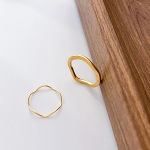 Detailed view of stacked minimalist gold wavy rings on wooden and white surface