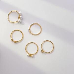 Detailed flat lay of gold rings set featuring pearls, twisted bands, and micro zircons