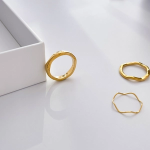 Detailed view of three stackable gold wavy irregular minimalist rings on a jewelry box