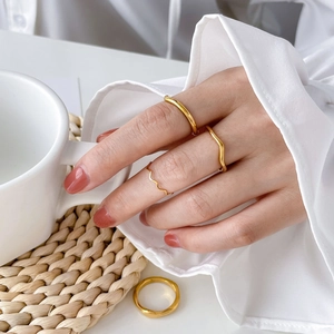 Close-up of golden wavy and smooth stackable rings worn on hand with minimalist aesthetic