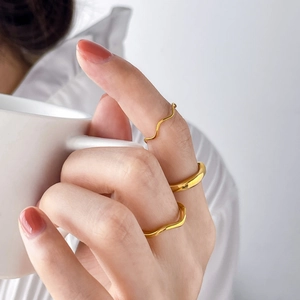 Three-piece set of minimalist wavy and thick golden rings worn on a hand holding a ceramic cup