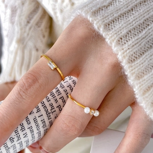 Detail of freshwater pearl and oval zircon gold rings worn on a hand with a knit sweater