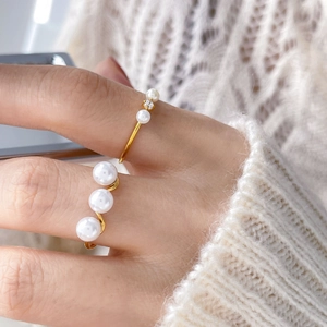 Close-up of golden pearl rings with small zircon on a model against white knitwear