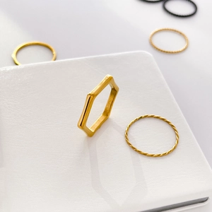Detail of minimalist golden hexagonal ring and twisted rope band on white display