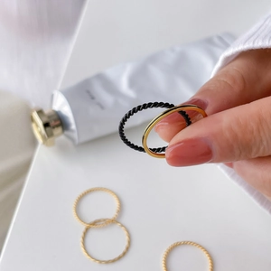 Detail of minimalist gold twist rings and black enamel hexagon rings stacked on a hand