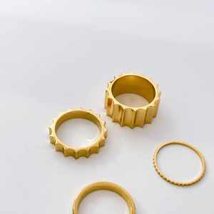 Close-up of four stacked 18K gold plated titanium rings with gear and wave patterns