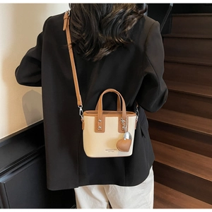Detail of two-tone bucket bag with leather texture, heart charm, and adjustable strap