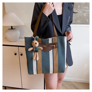 Close-up of vintage striped canvas tote bag with brown faux leather pocket and rabbit charm