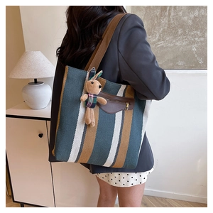 Detail of striped canvas tote bag featuring leather front pocket and plush bunny pendant