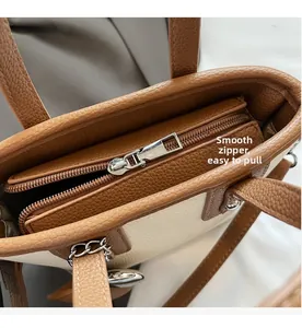 Detail view of smooth metal zipper and brown leather trim on a large beige bucket bag