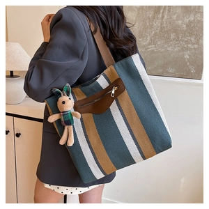 Detail of striped canvas tote bag with a small plush rabbit pendant and leather pocket
