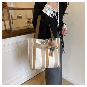 Detail of striped canvas tote bag with decorative leather patch and plush bunny charm