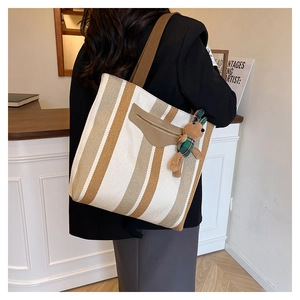 Detail of striped canvas tote bag featuring brown leather pocket and rabbit plush charm