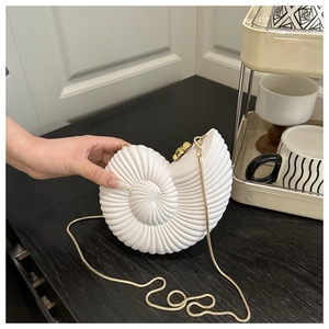 Detailed close-up of white seashell clutch bag with gold chain and spiral texture