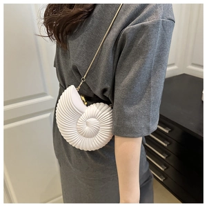 Close-up of white seashell cross-body bag with golden chain and metallic ball clasp