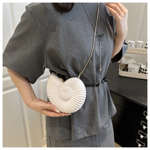 Detail of white conch-shaped crossbody bag with acrylic gold chain on a model