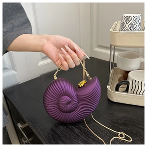 Macro view of purple conch-shaped shell clutch with gold chain and spiral texture