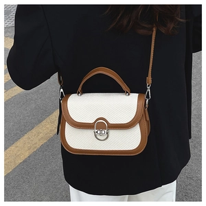 Detail of a brown and white patchwork crossbody bag showing stitching and silver metal clasp