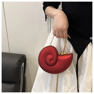 Detail of red snail-shaped shell clutch bag with gold chain strap held by a model