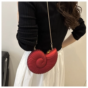 Detail of red conch shell crossbody bag with spiral texture and golden snake chain strap