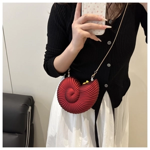 Detail of red conch-shaped crossbody bag with gold chain strap on a person