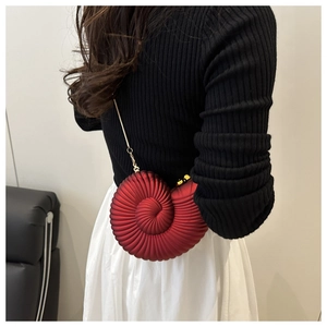 Detail of red conch-shaped shoulder bag with gold chain strap on a black sweater