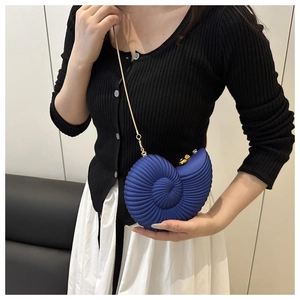 Detail of dark blue shell-shaped crossbody bag with gold chain strap on model